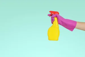 hand with pink gloves holding a yellow disinfectant spray bottle