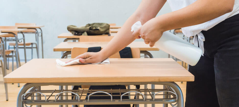 person spraying disinfectant on a classroom student desk